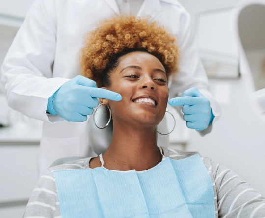 Dentist in blue gloves examining smiling patient's teeth in dental office.