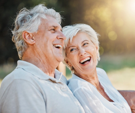Happy senior couple smiling outdoors in natural sunlight, promoting dental health and wellness.
