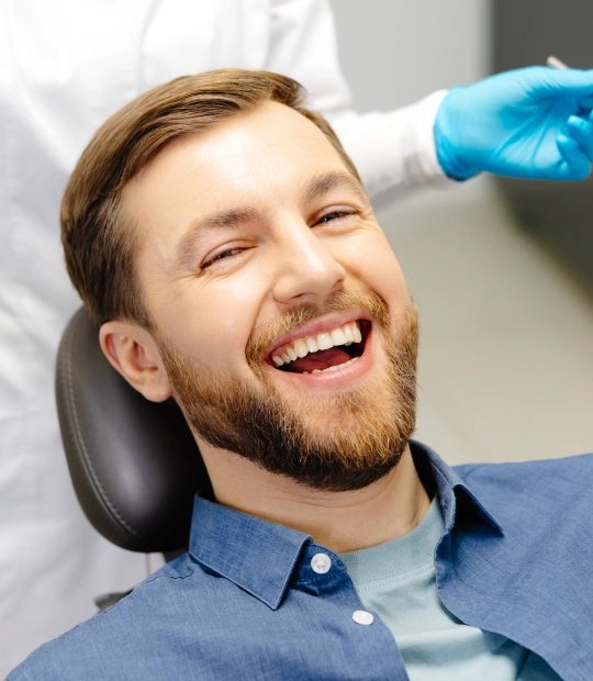 Man smiling during dental examination in dentist's office with gloved dentist present.