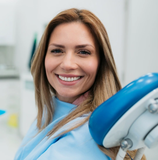 Smiling dental professional in blue scrubs holding dental equipment in modern clinic setting.