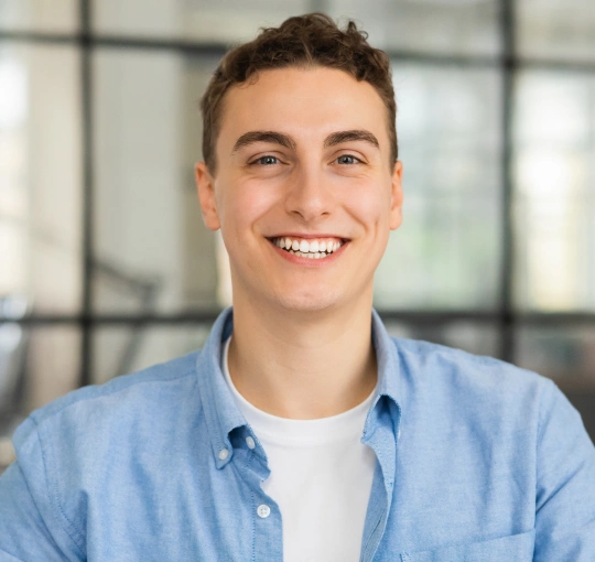 Young man smiling at camera wearing light blue shirt in modern dental office setting.