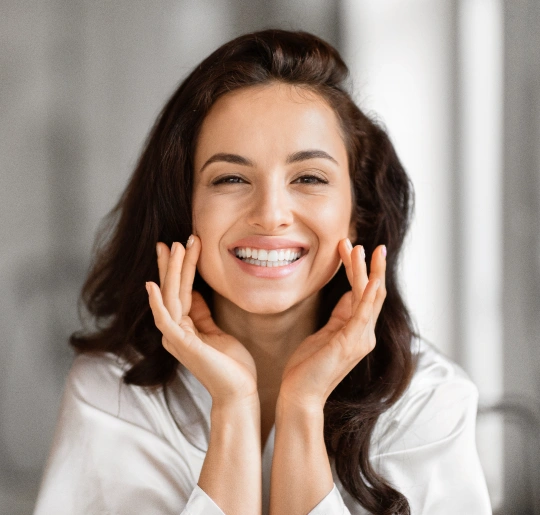 Smiling woman with hands to face in bright dental office setting, promoting dental care services.