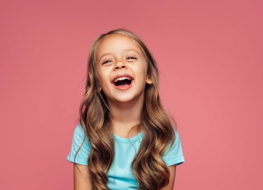 Happy young girl with bright smile against pink background for pediatric dentistry website