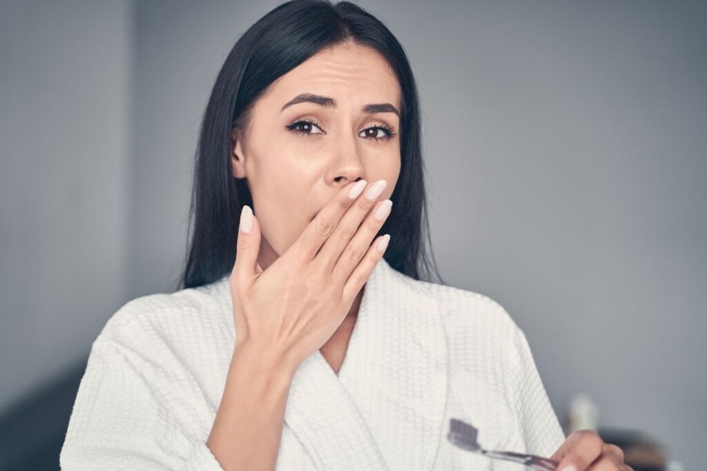 concerned woman covering her mouth while holding a toothbrush
