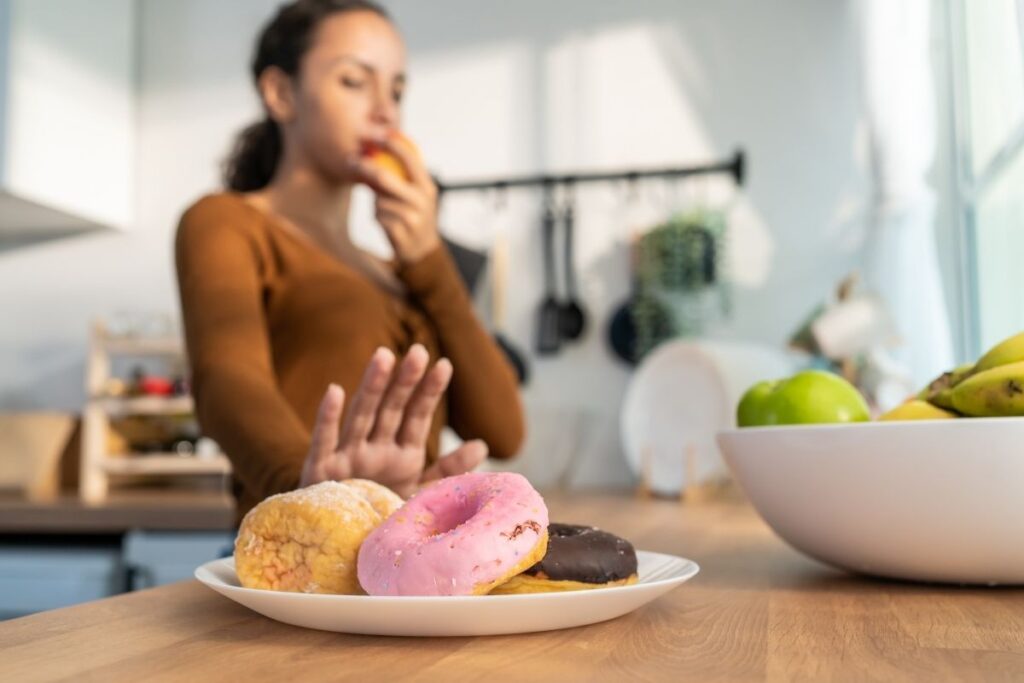 Woman choosing a healthy apple instead of sugary donuts, demonstrating a tooth-friendly diet for better oral health.