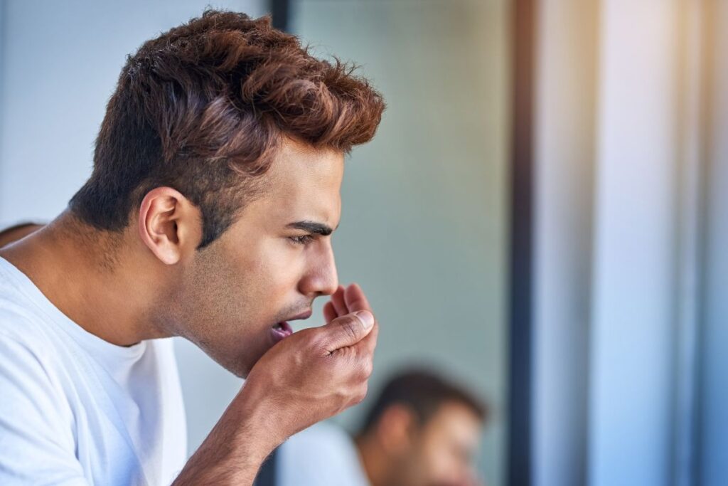 A man covers his mouth while checking his breath, illustrating concern about persistent bad breath as a possible oral health issue.