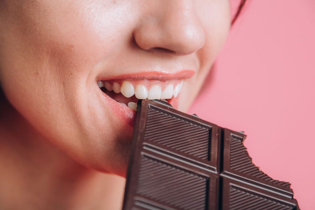 Close-up of a woman biting a piece of dark chocolate, highlighting a common food that can stain teeth after whitening treatment